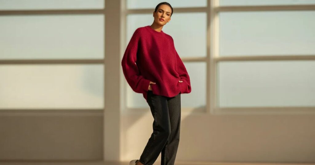 Man wearing a fitted red jumper with dark jeans and leather boots at a rooftop bar.